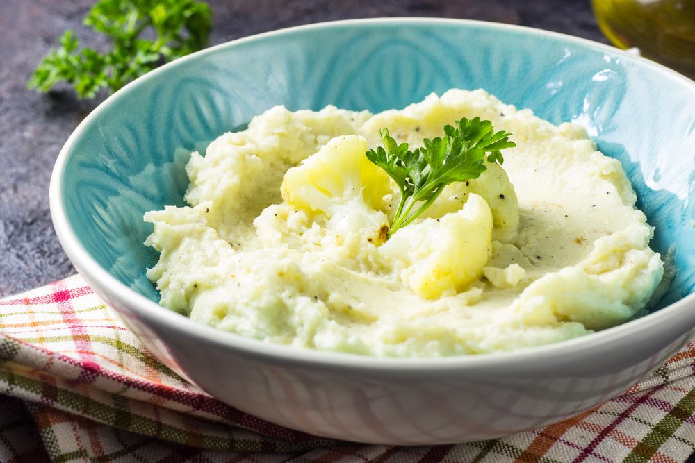 A bowl of mashed potatoes with parsley on the side.