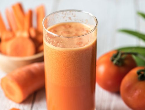 A glass of carrot juice with some other vegetables in the background.