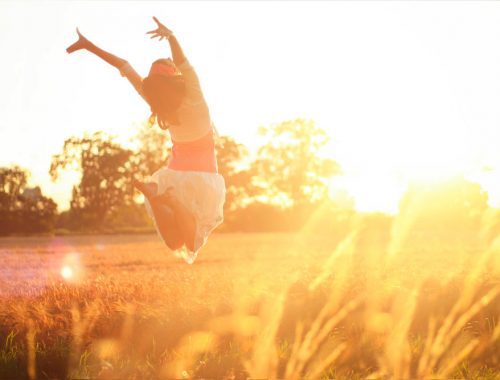 A woman jumping in a field at sunset.