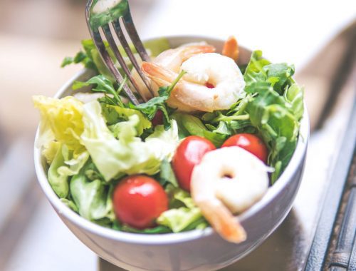 A salad with shrimp and tomatoes in a white bowl.