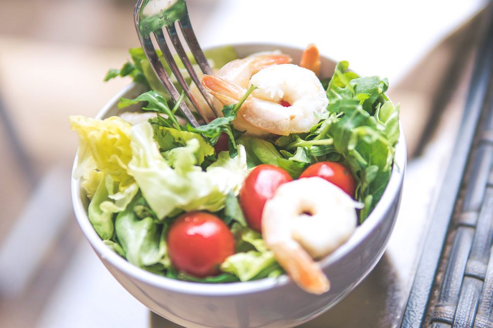 A salad with shrimp and tomatoes in a white bowl.