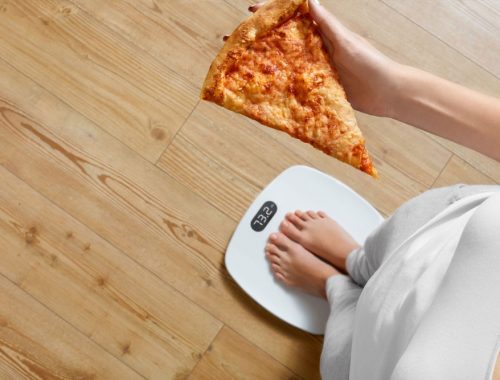 A woman is holding a slice of pizza on a scale.