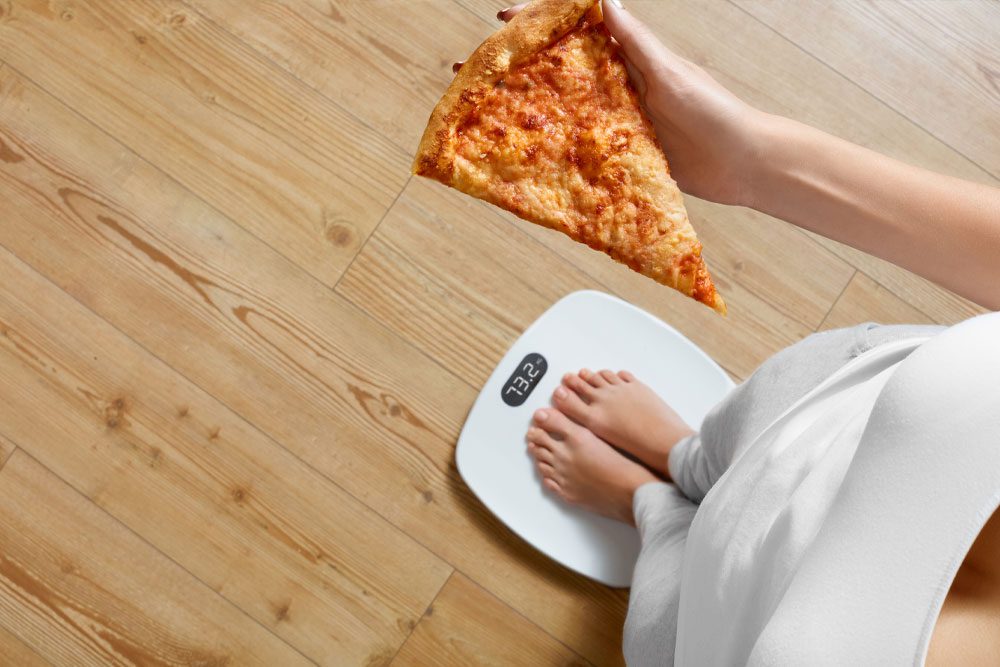 A woman is holding a slice of pizza on a scale.
