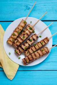 A plate of grilled meat on wooden skewers.