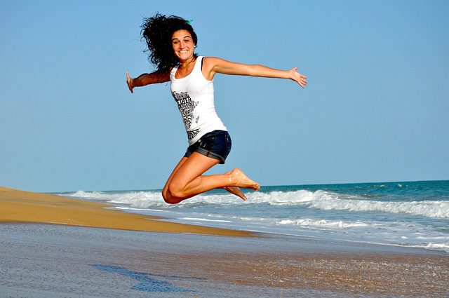 A woman jumping in the air on top of a beach.